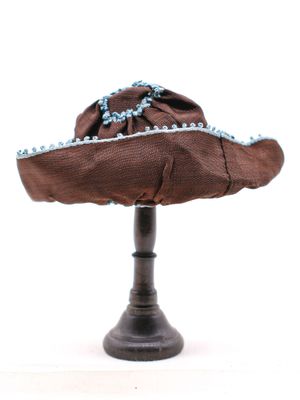 un chapeau marron orné de perles bleues, posé sur un présentoir