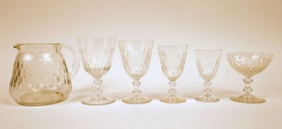 six verres à vin et un pichet sont alignés sur une surface blanche