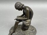 bronze statue of a boy sitting on a rock reading a book