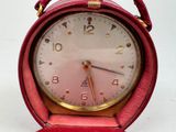 a red alarm clock sitting on a stand on a white surface