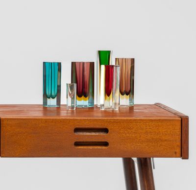 plusieurs vases en verre de différentes couleurs posés sur une table en bois, sur fond blanc