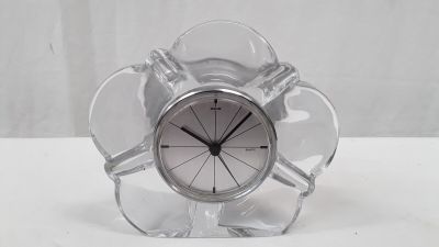 une horloge en verre transparent avec un cadran argenté, posée sur une table blanche