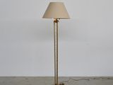 a brass floor lamp with a beige shade on top of it