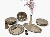 a vase with a flower in it next to a bunch of silver plates