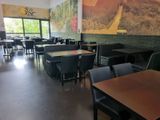 tables and chairs in a restaurant with a large painting on the wall