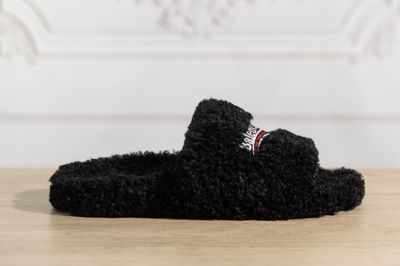 des chaussons noirs duveteux posés sur une table en bois, avec un mur blanc en arrière-plan