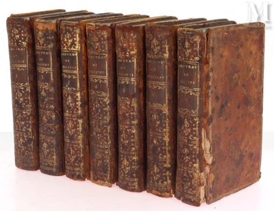 six old books are lined up in a row on a white surface