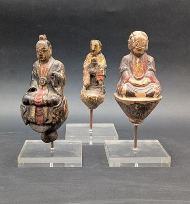 trois figurines asiatiques représentant des bouddhas, exposées sur des socles en acrylique transparent