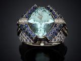 a close up of a ring with a large green stone surrounded by blue and white sapphires