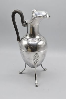 an antique silver plated pitcher on stand with a black handle