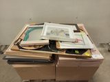 une pile d'œuvres d'art encadrées posées sur une palette dans une pièce