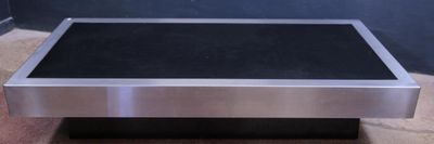 table basse en acier inoxydable avec un plateau en verre noir posée sur un parquet