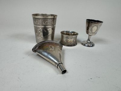 trois tasses en argent et un entonnoir en argent posés sur un plateau blanc