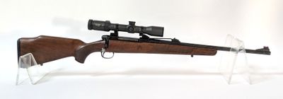 le fusil est posé sur un support transparent équipé d'une lunette de visée
