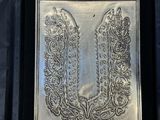 an ornate silver plaque on a black cloth with a black background