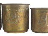 four antique brass canisters are lined up against a white background