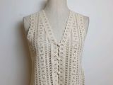 Le gilet est tricoté avec du fil blanc et présente un motif au crochet sur le devant.