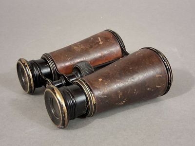 une paire de jumelles d'aspect ancien posée sur une table, sur fond gris