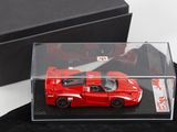 une petite voiture rouge dans une boîte transparente posée sur un tissu noir