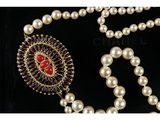 a close up of a necklace with pearls and a red stone