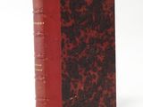 an old book with a red cover sitting on top of a white surface