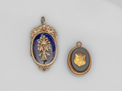 deux pendentifs en verre doré et bleu, l'un représentant un lion et l'autre un médaillon
