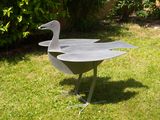 a metal sculpture of a bird on a stand in the grass