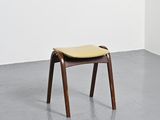 an image of a wooden stool with a yellow seat in a white room
