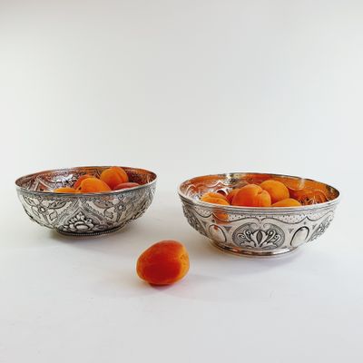two silver bowls with oranges in them on a white surface