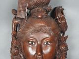 une image représentant une sculpture en bois représentant le visage d'une femme avec un oiseau sur la tête