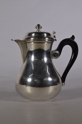 une cafetière ancienne en argent avec une poignée noire, posée sur une table