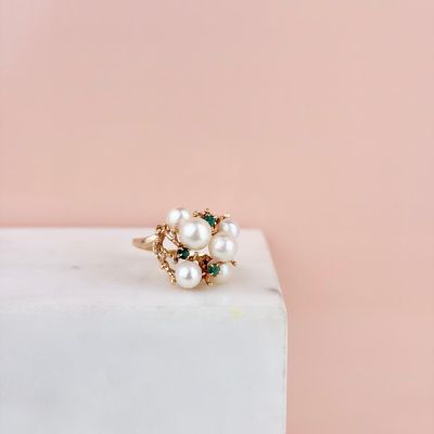 un gros plan d'une bague en or ornée de perles, posée sur un bloc de marbre