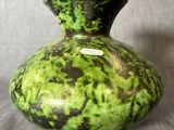 un vase vert et noir posé sur une surface grise