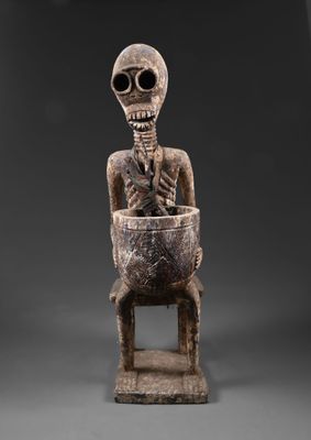 une statue représentant un squelette assis sur une chaise en bois
