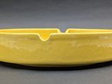 yellow ceramic ashtray with a curved edge on a gray background
