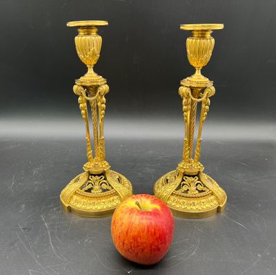 deux bougeoirs dorés posés à côté d'une pomme sur une table