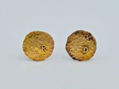 paire de boucles d'oreilles plaquées or, ornées d'initiales sur un fond blanc