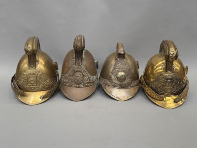 trois casques de pompier anciens en laiton, posés côte à côte sur une surface grise