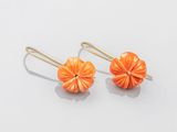 une photo représentant une paire de boucles d'oreilles orange posées sur une surface blanche