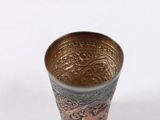 a silver cup with a design on it sitting on a white surface