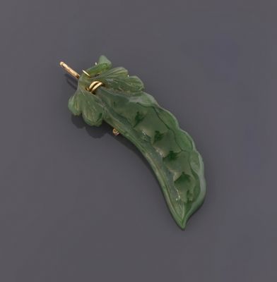 une image représentant une broche en forme de feuille de jade vert posée sur une surface noire