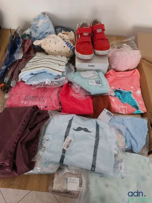 une boîte remplie de vêtements et une paire de chaussures par terre