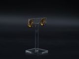 a pair of gold earrings on a clear stand against a black background