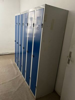 Plusieurs casiers bleus sont alignés contre un mur dans une pièce vide.