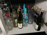many bottles and glasses on the shelf of a cabinet