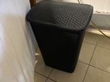 a black trash can next to a white towel on a rack
