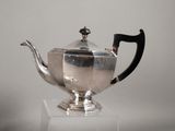 a silver teapot with a black handle on a white pedestal