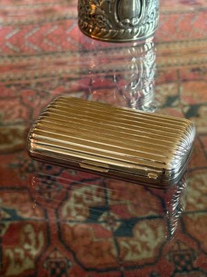 a silver cigarette case sitting on a table next to a vase