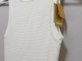 white knitted tank top hanging on a hanger in front of a white wall