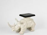 une statue de rhinocéros blanc coiffé d'un chapeau noir, assis sur une surface blanche